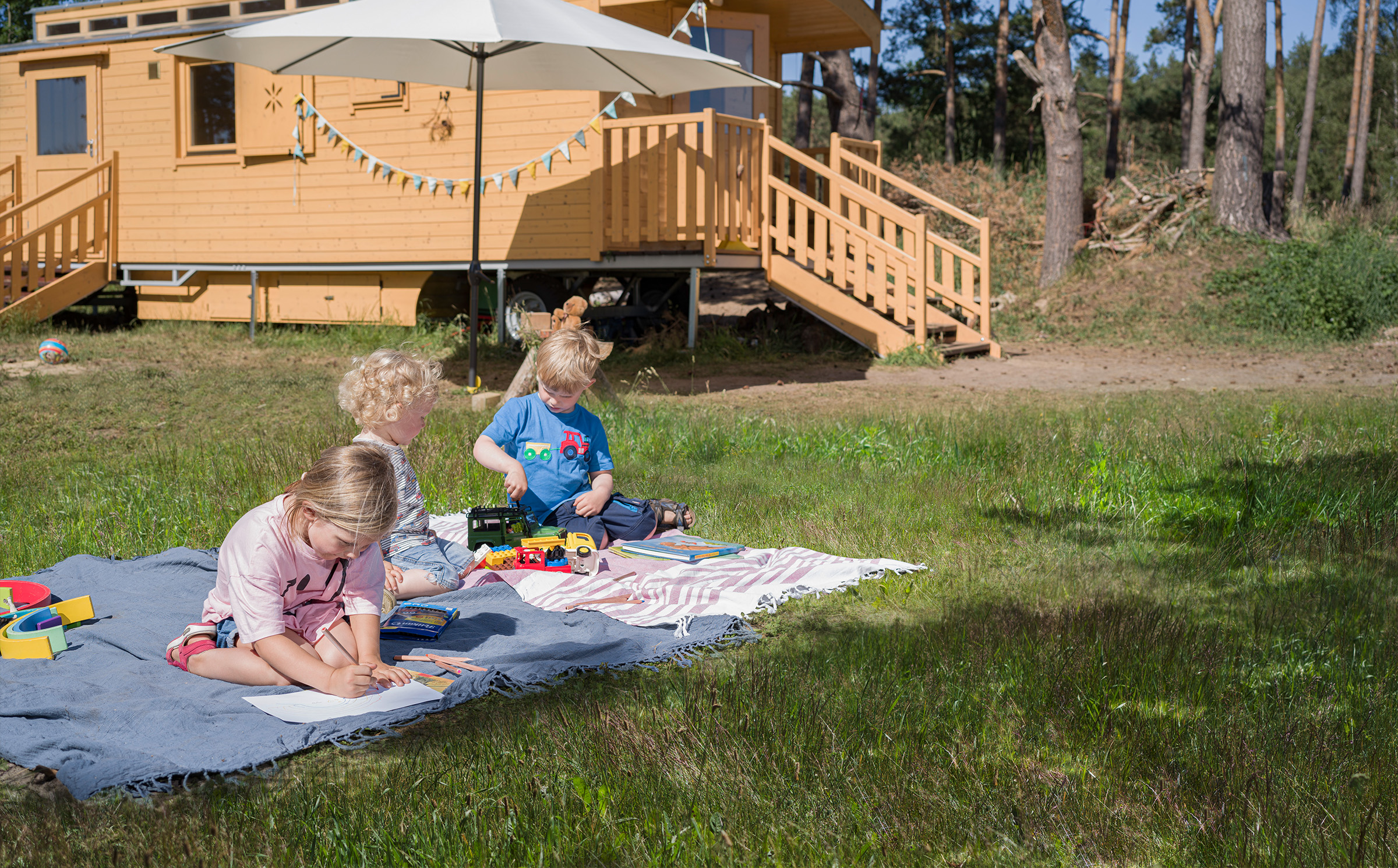 Kinder auf einer Picknickdecke vor einem NAWALO Waldkindergartenwagen mit Terrasse