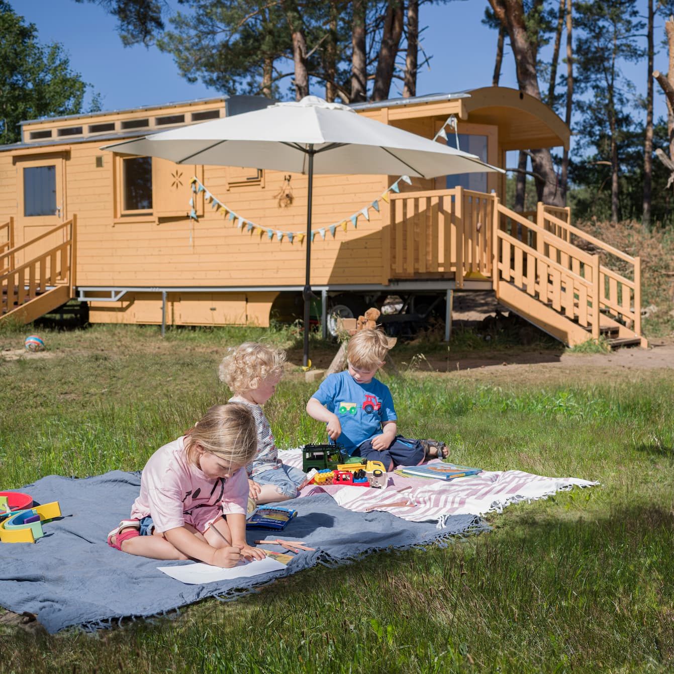 Kinder auf einer Picknickdecke vor einem NAWALO Waldkindergartenwagen